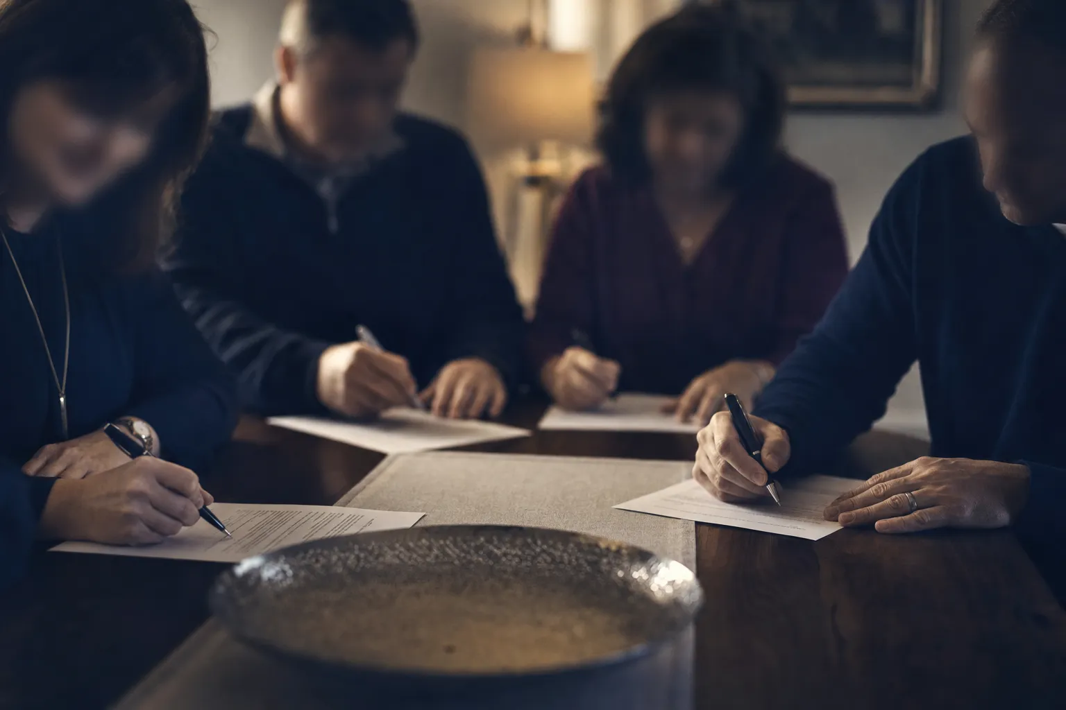 Family members signing beneficiary consent forms around a dining table